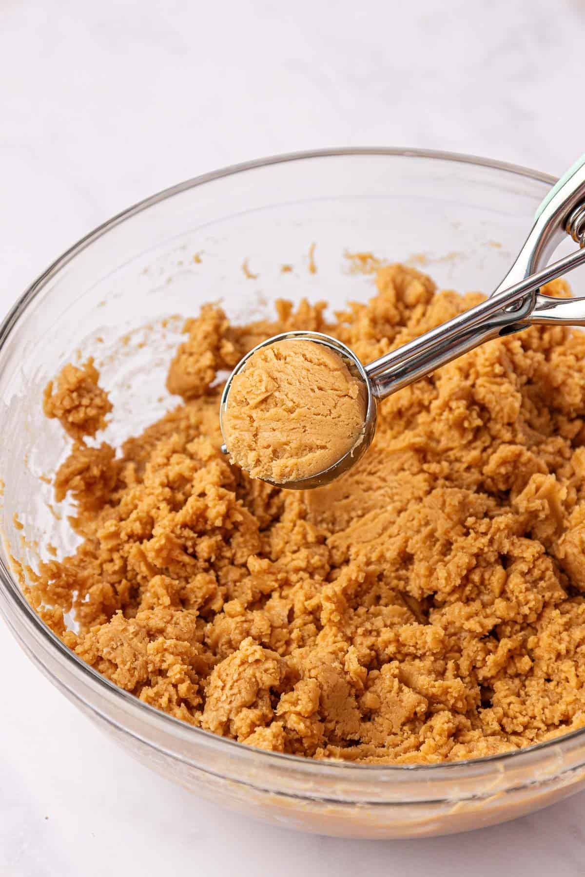scooping peanut butter cookie batter from a mixing bowl
